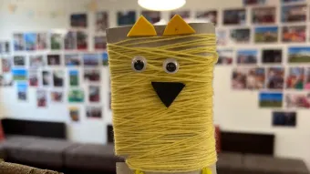 Kinder haben aus einer Kartonrolle eine gelbe Eule gebastelt.